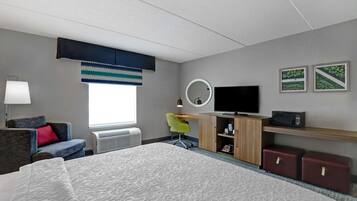 Quarto de hotel com cama, escrivaninha, cadeira, televisão, espelho e janela com persianas.