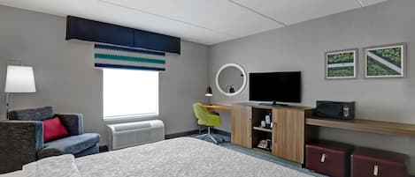 Une chambre d’hôtel équipée d’un lit, d’un bureau, d’une chaise, d’une télévision, d’un miroir et d’une fenêtre avec des stores.