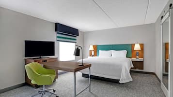 A hotel room with a bed, a desk with a chair, a television, and a window with blinds.