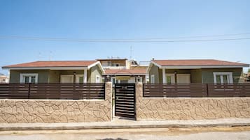 A gated residential area with two houses, a stone wall, and a clear sky.