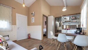 A compact living space with a sofa, dining table, and chairs, a kitchenette with a microwave and sink, and a door leading to a bedroom. - Olympia's Apartments (Spata-Artemida)