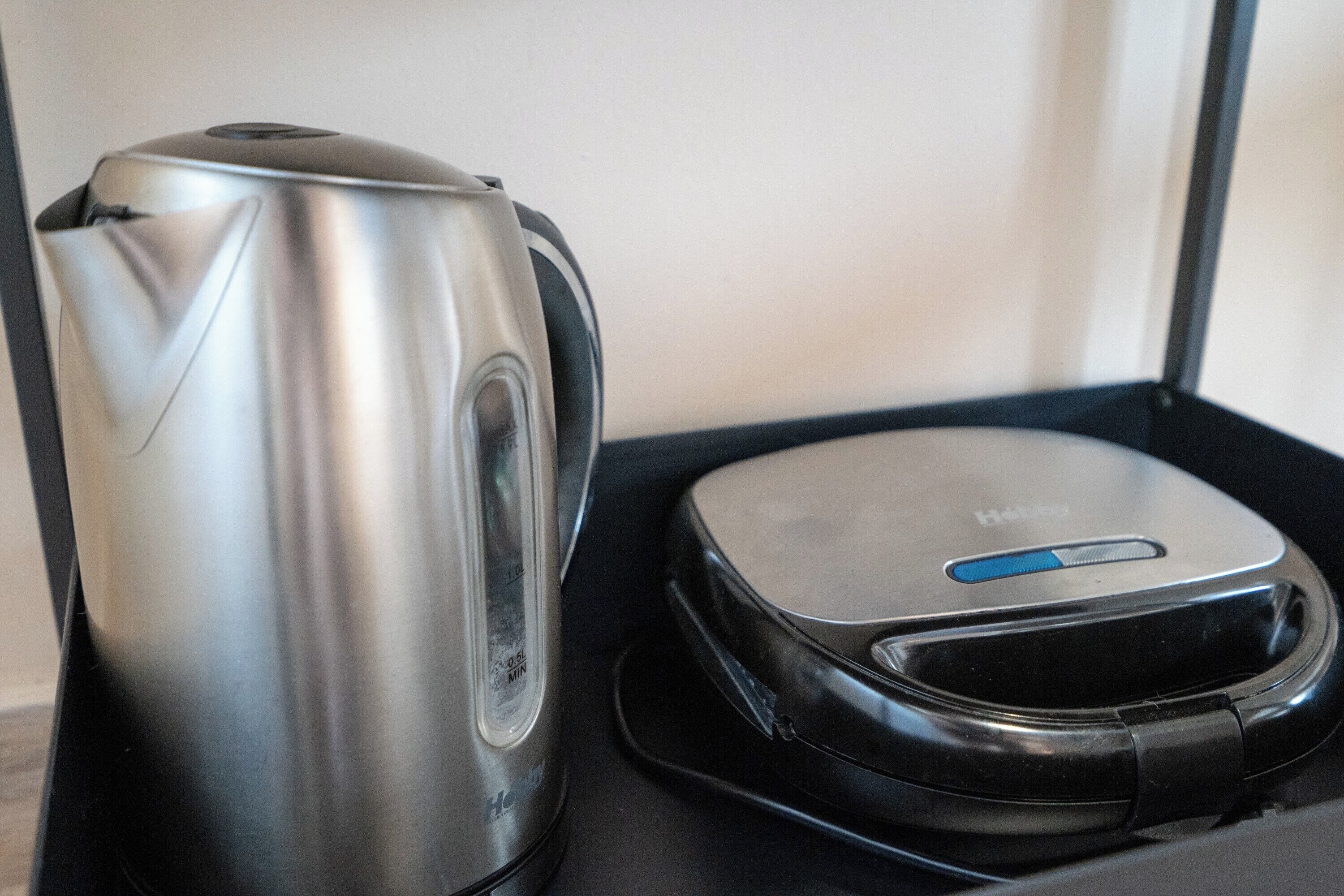 Uma chaleira de aço inoxidável e um dispositivo eletrônico preto compacto sobre uma bandeja preta.