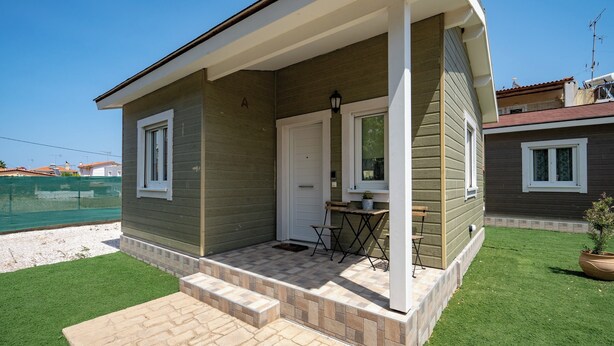 A single-story house with a covered porch, a small table, and a chair. - Olympia's Apartments (Spata-Artemida)