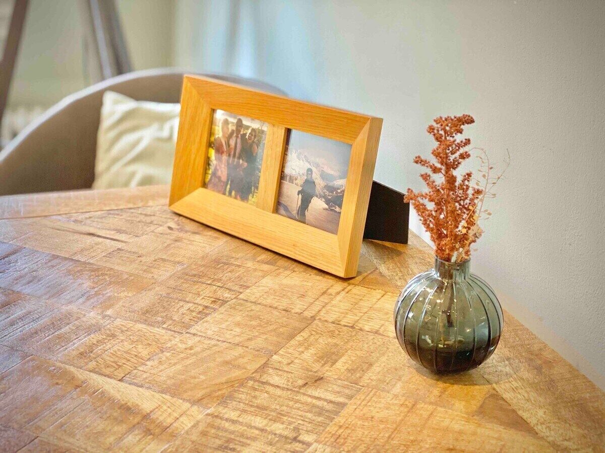 Une table en bois sur laquelle sont posés un cadre photo et un vase en verre transparent contenant des fleurs séchées.