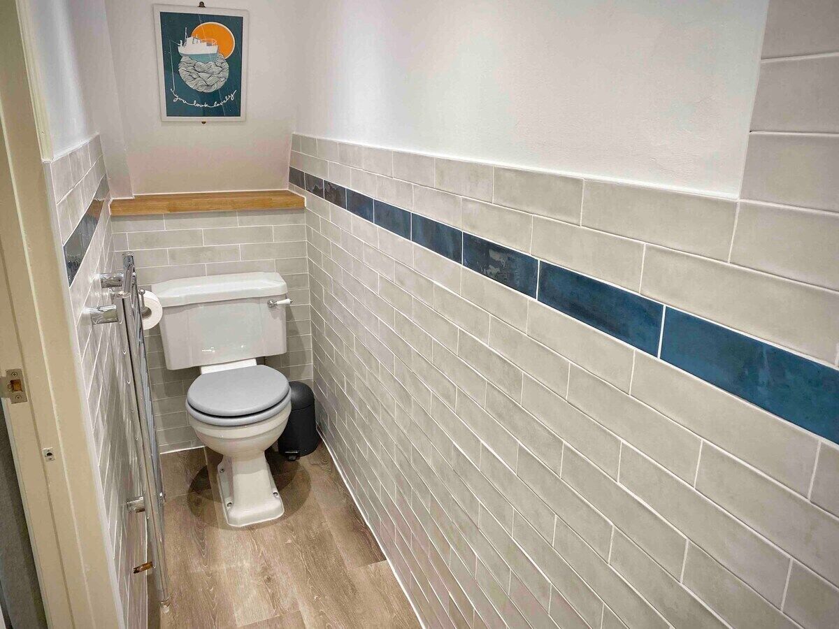 A small bathroom with a toilet, a trash bin, and a wall-mounted toilet paper holder.