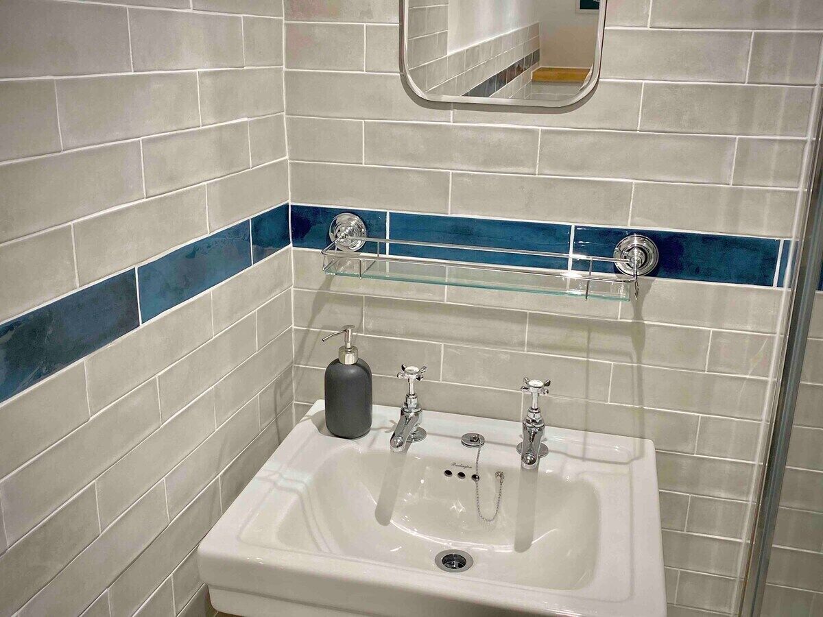 A bathroom with a white sink, two faucets, a soap dispenser, and a glass shelf.