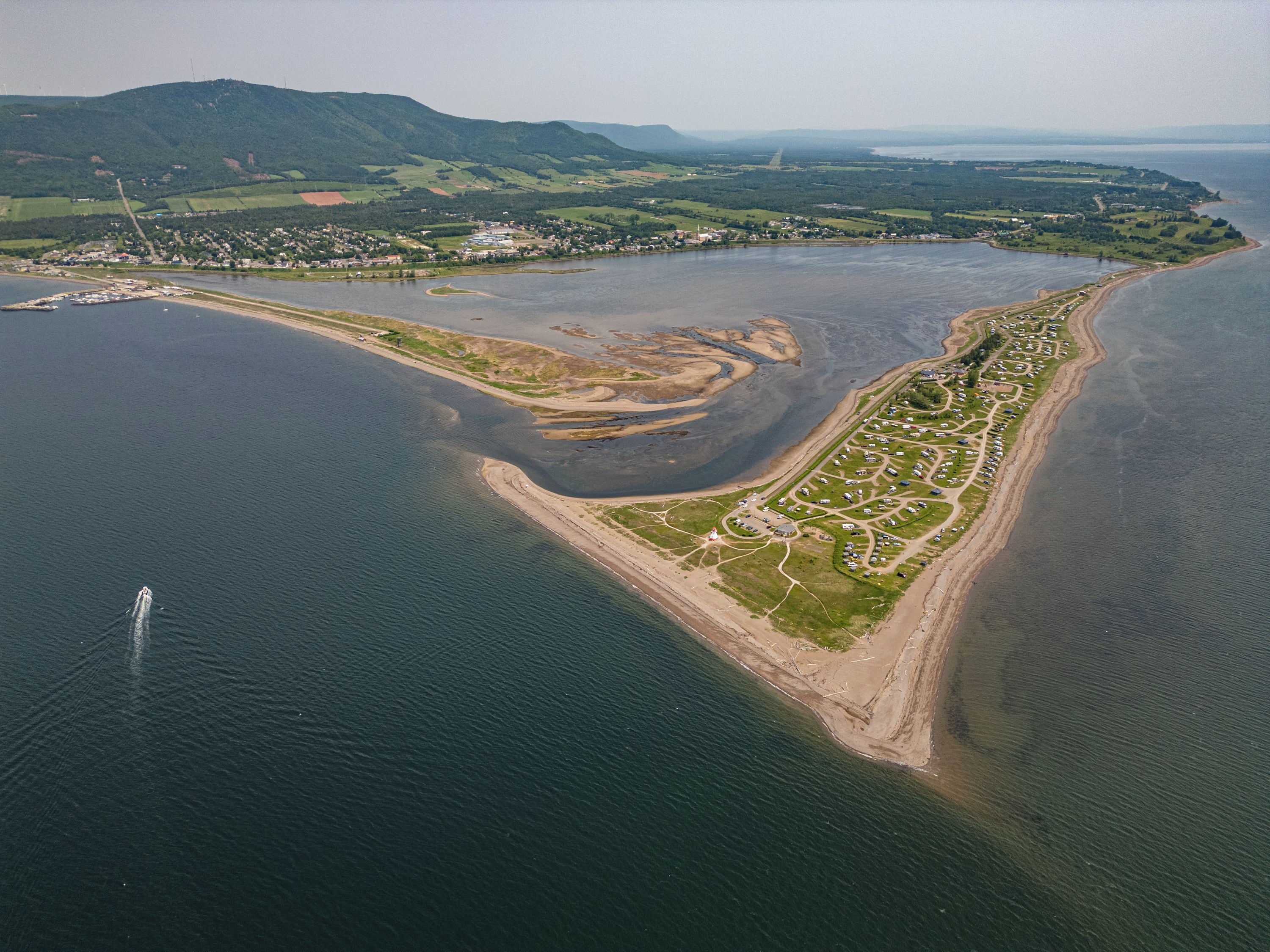 An aerial view of a coastal area with a marina, a residential zone, and a hilly landscape in the background.