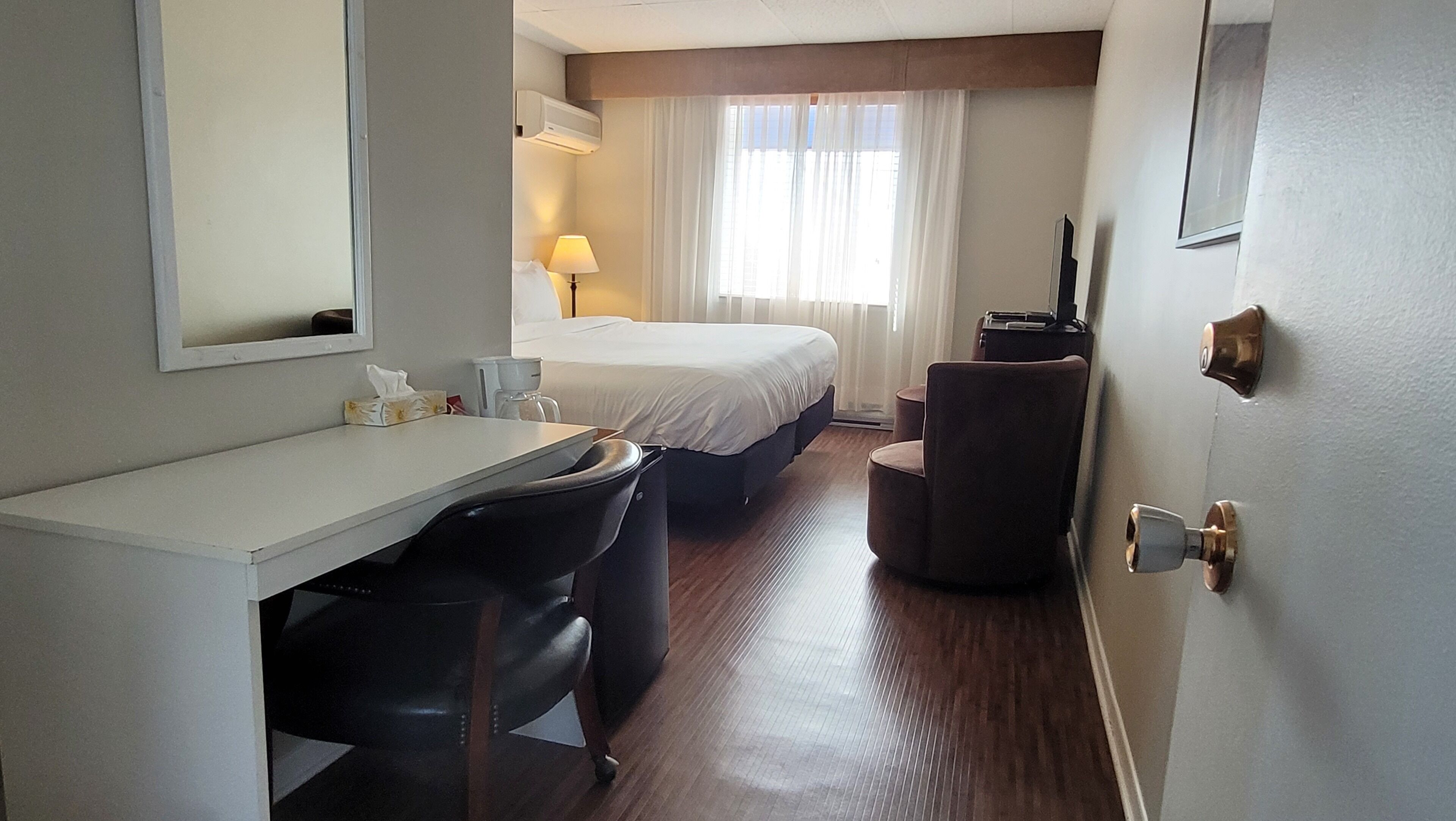 A hotel room with a bed, a desk with a chair, a lamp, and a television.