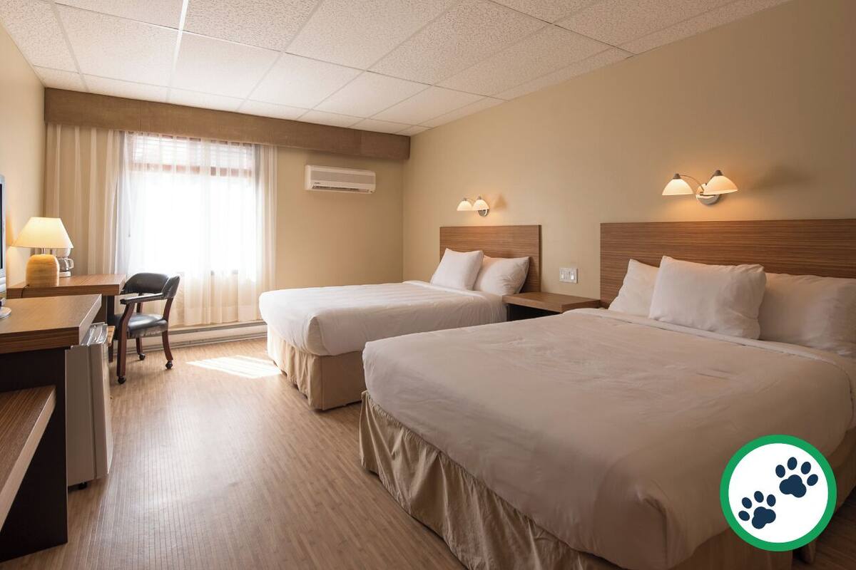Ein Hotelzimmer mit zwei Betten, einem Schreibtisch, einem Stuhl und einem Vorhangfenster.