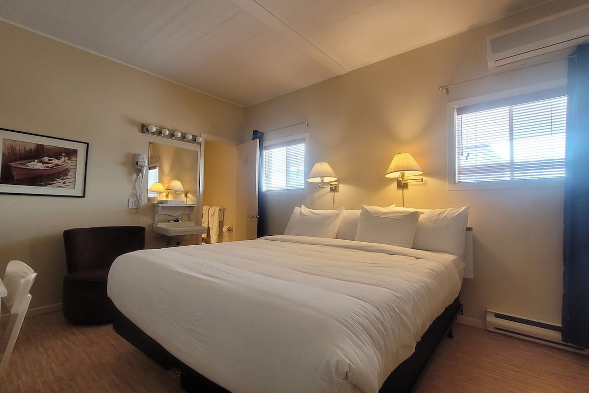 Ein Hotelzimmer mit Bett, Nachttischlampen, einem Spiegel, einem Waschbecken und einem gerahmten Bild an der Wand.