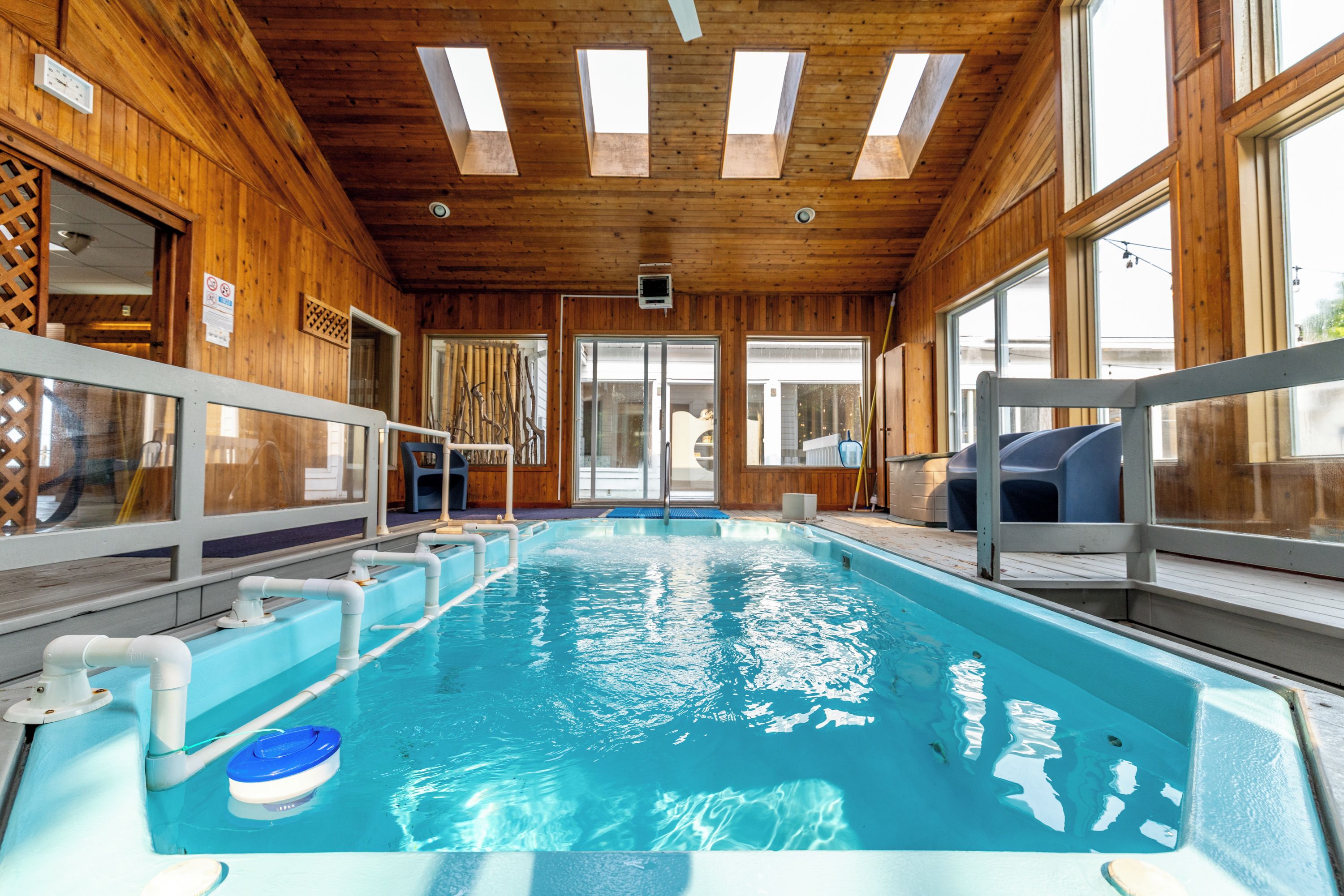 En indendørs swimmingpool med klart vand, trævægge og et loft med ovenlys.