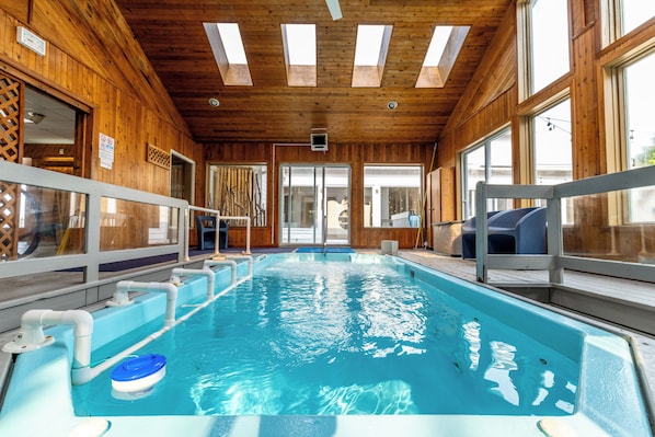 An indoor swimming pool with clear water, wooden walls, and a ceiling with skylights.