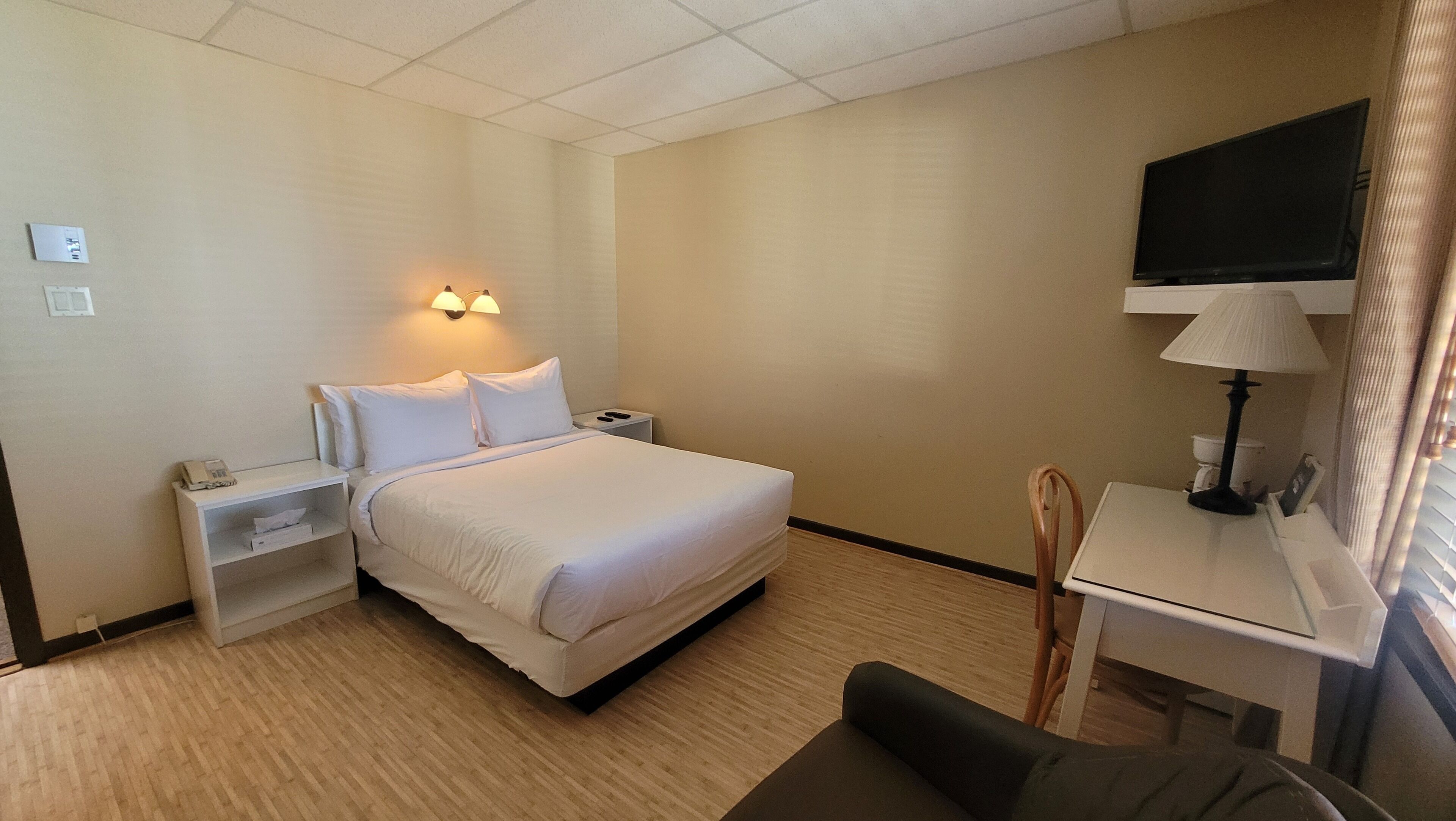 A hotel room with a bed, bedside tables, a desk with a lamp, a chair, and a TV on the wall.