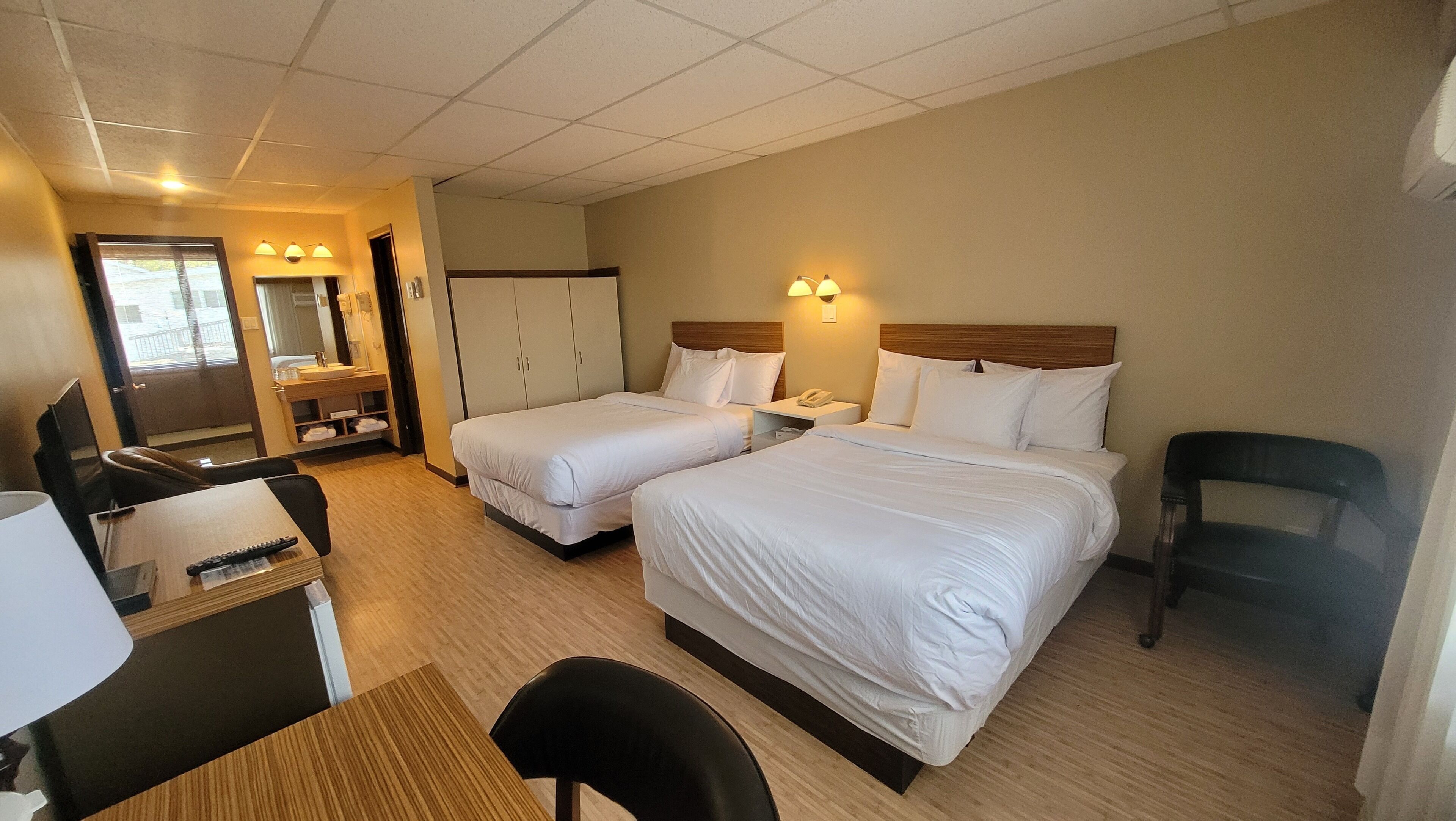 Hotellihuone, jossa on kaksi sänkyä, työpöytä, tuoli, vaatekaappi sekä kylpyhuone, jossa on peili ja pesuallas.