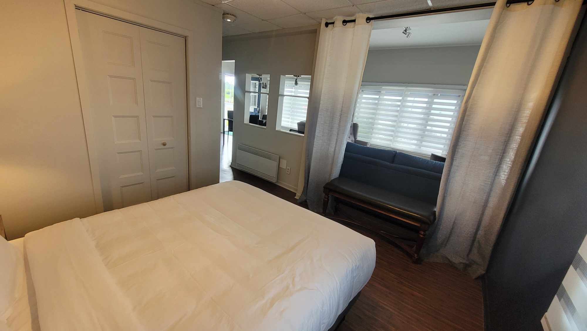 Habitación de hotel con cama, un banco, una ventana con persianas y una puerta.