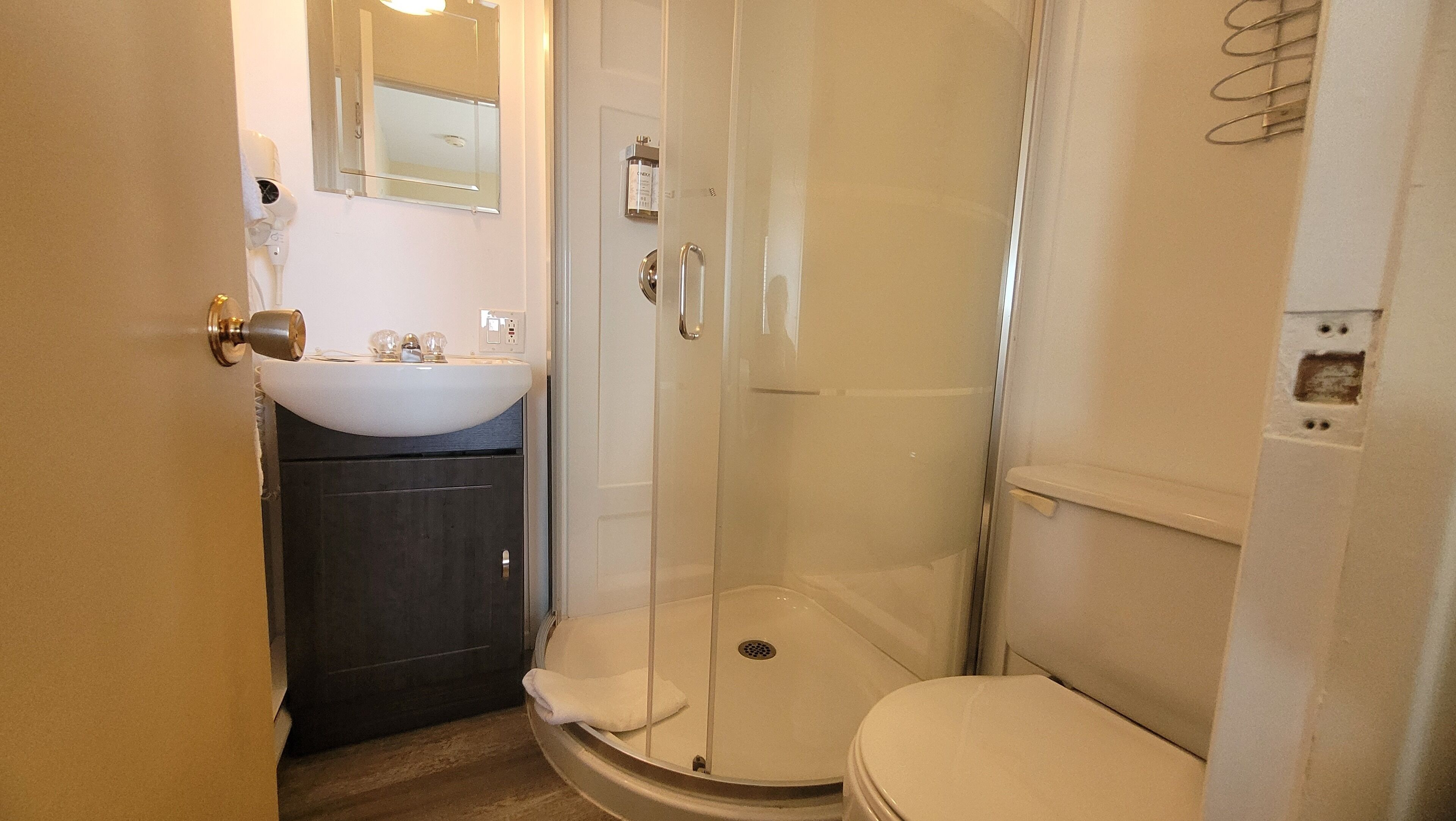 Un bany petit amb un lavabo blanc, un vàter i una dutxa amb portes de vidre.