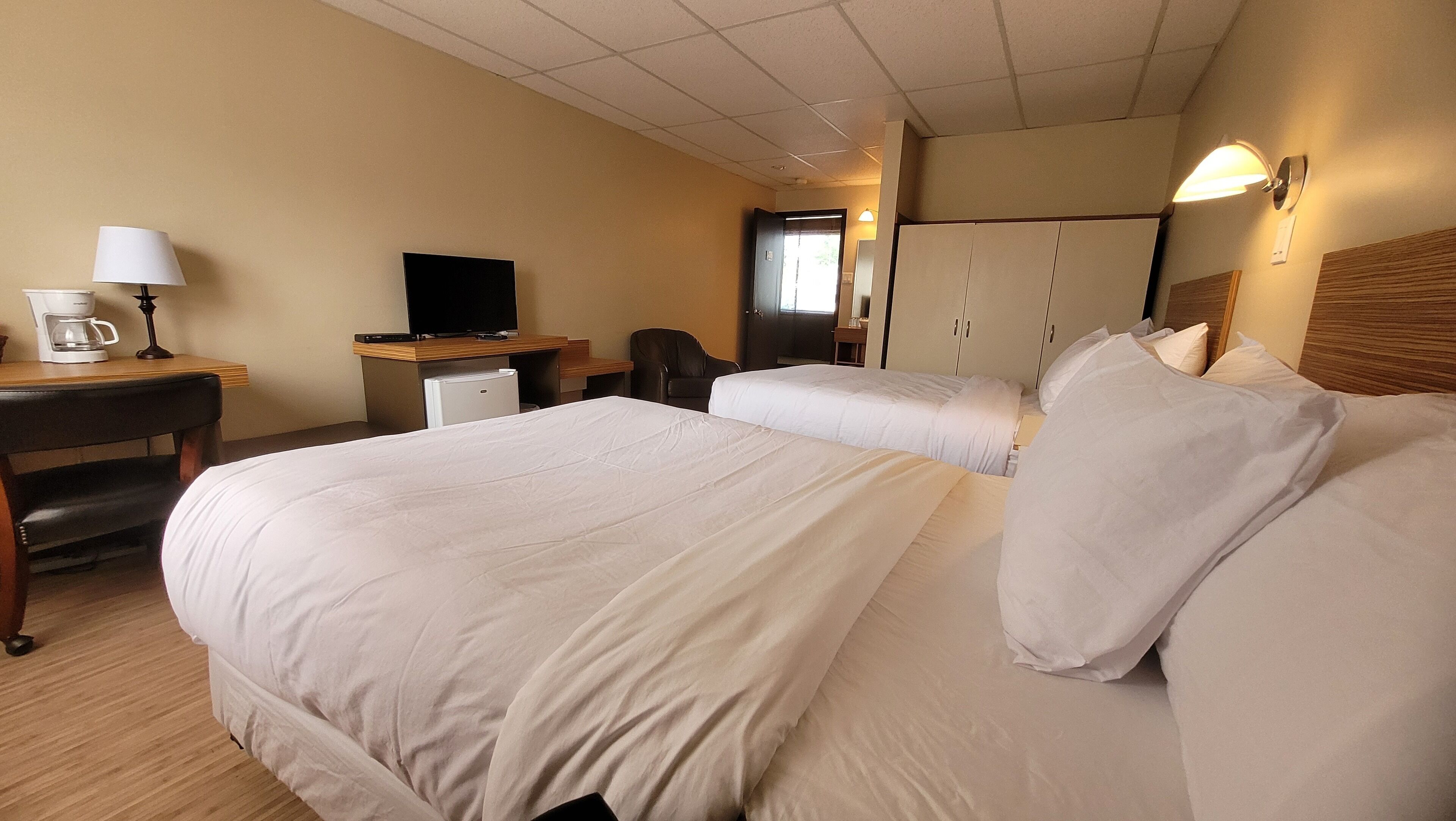 A hotel room with two beds, a desk with a lamp, a coffee maker, a TV, and a wardrobe.