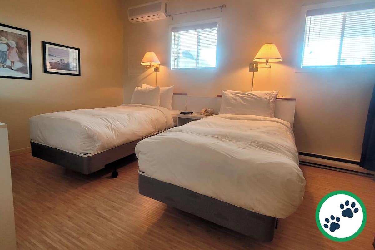 Ein Hotelzimmer mit zwei Betten, Holzboden und zwei Wandlampen.