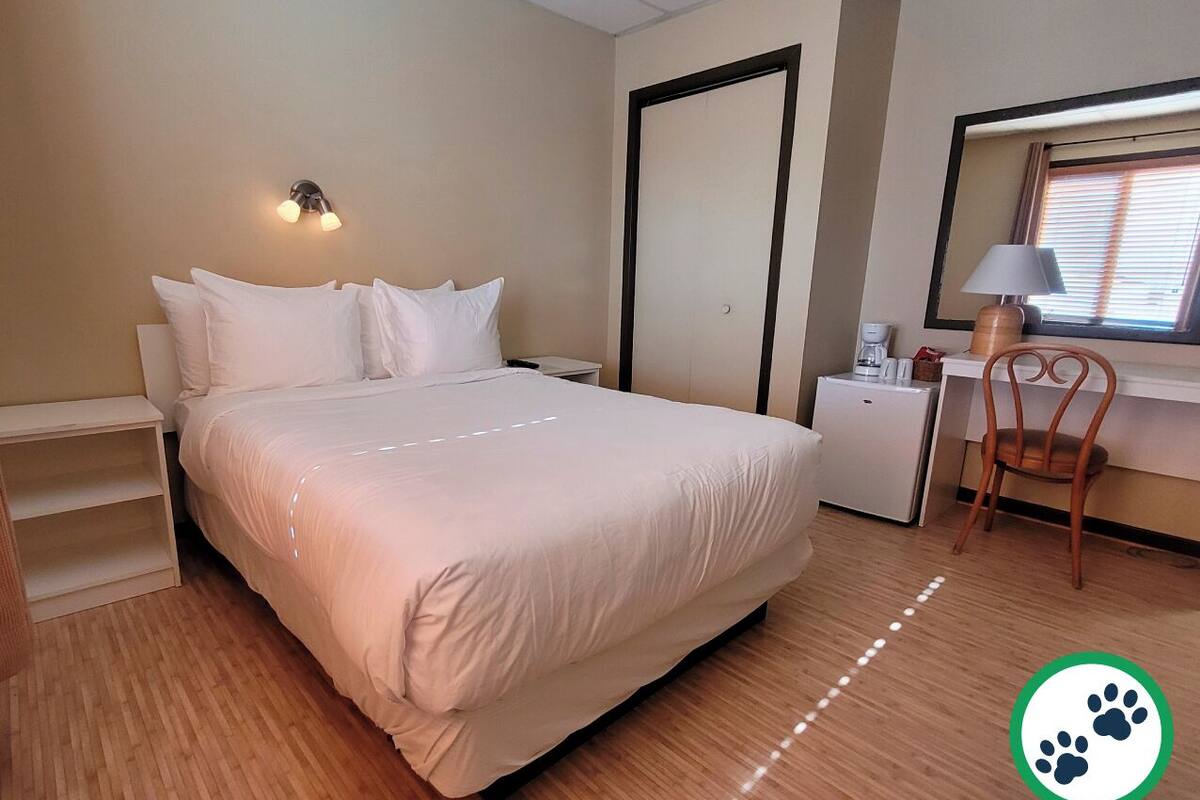 Ein ordentlich eingerichtetes Schlafzimmer mit Bett, Nachttisch, Stuhl und einem Fenster mit Jalousien.
