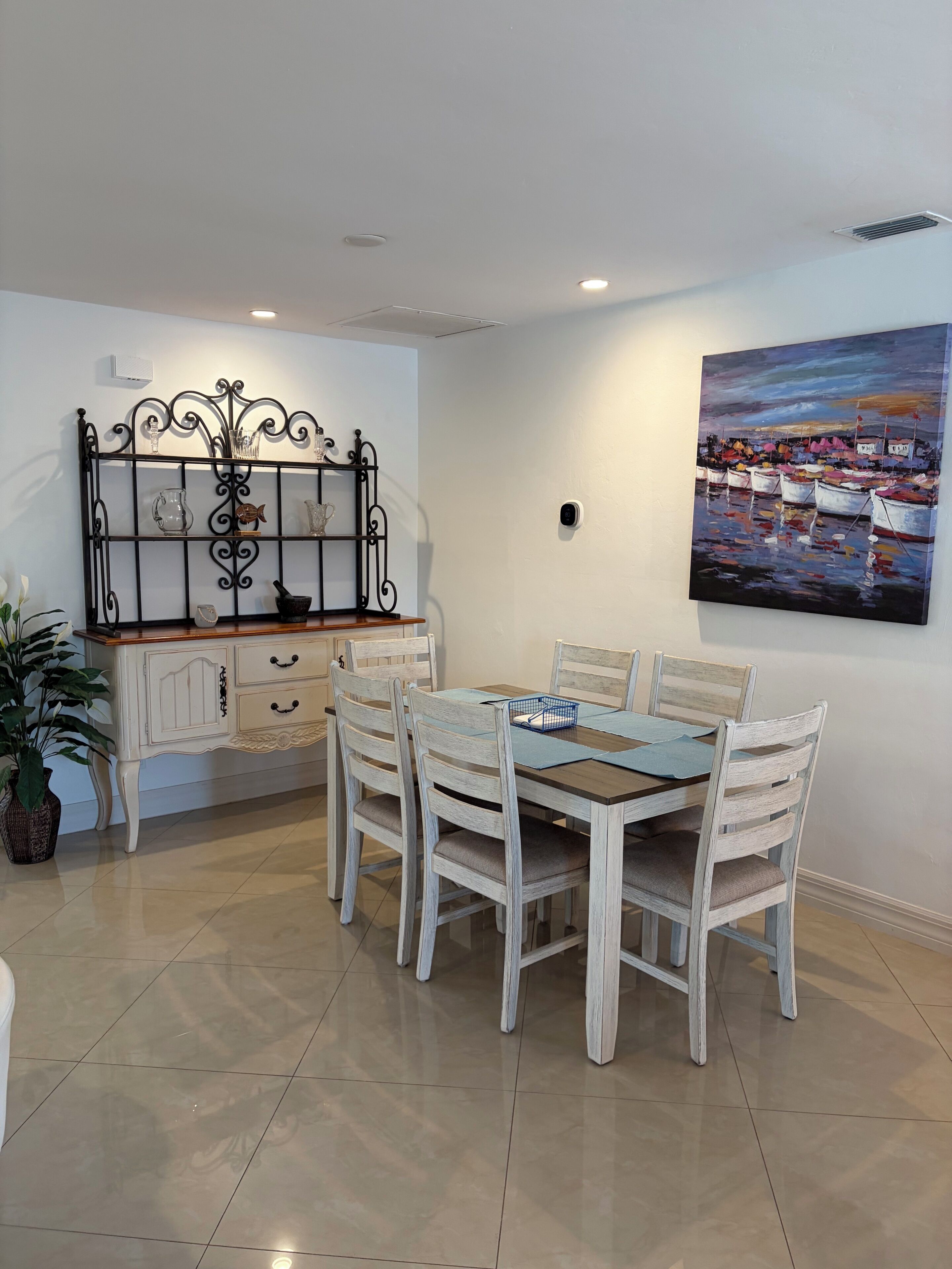 A dining area with a table, chairs, a decorative metal headboard, and a painting on the wall.