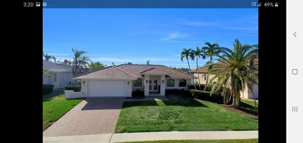 A single-story house with a front lawn, a driveway, and a clear blue sky.