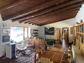 A spacious living room with a high wooden ceiling, a dining table, chairs, a sofa, and a bookshelf.
