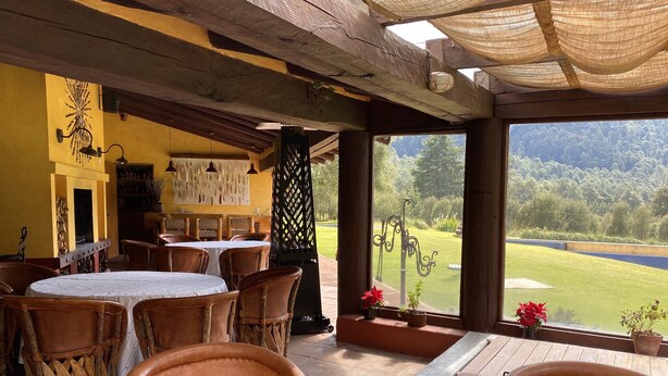 Un patio al aire libre con mobiliario de madera, vista a un campo de golf, e interior rústico con paredes amarillas y vigas de madera.