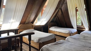 Un dormitorio rústico en el desván con camas de madera y una mesa, ventanas amplias con cortinas blancas y un techo inclinado.