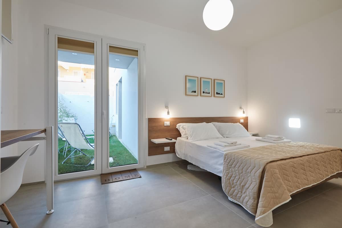 A bedroom with a bed, a desk, and a chair. There is a sliding glass door leading to a balcony.