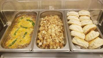 A buffet with three trays of food: a casserole with cheese and green peppers, a tray of diced potatoes, and a tray of biscuits.