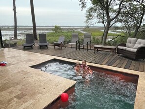 A swimming pool with a view of a water body, deck chairs, and a sofa.