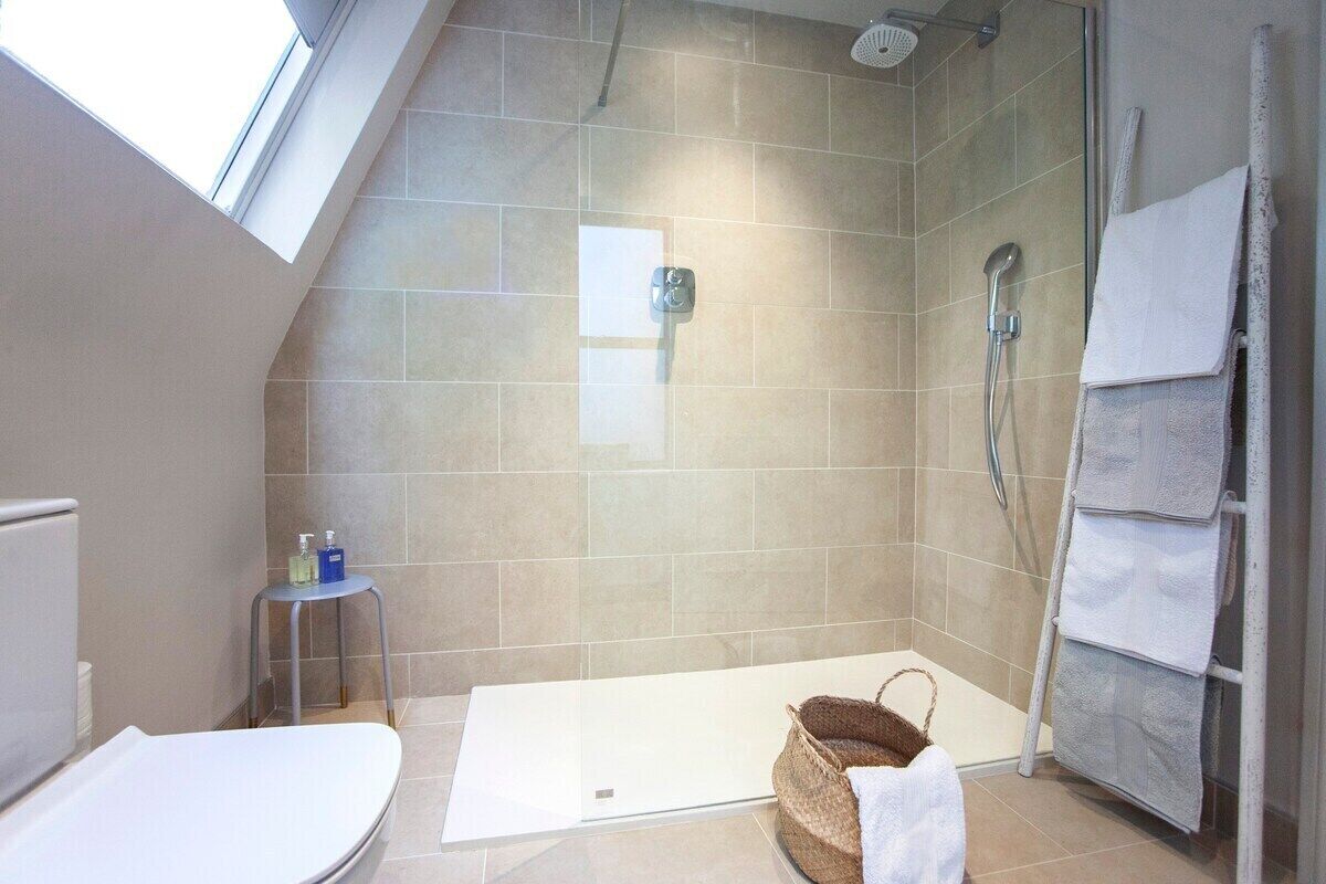 A modern bathroom with a shower, a toilet, and a small stool with toiletries.