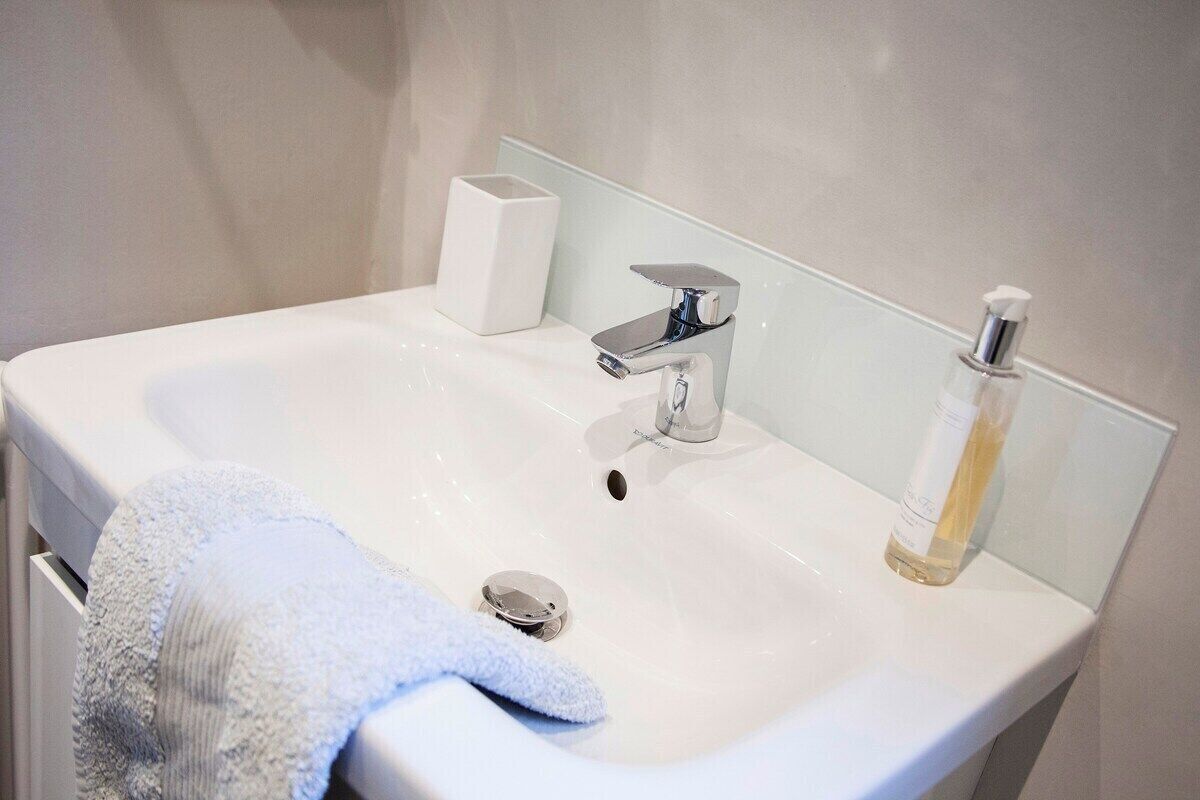 Un lavandino da bagno bianco con un rubinetto moderno, un erogatore di sapone e un asciugamano appeso al lato.