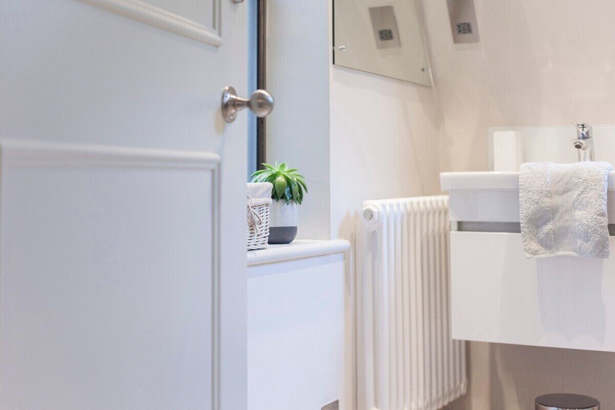 A bathroom with a white radiator, a towel hanging on the wall, and a potted plant on a shelf.