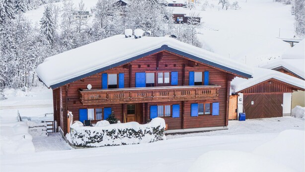 Een houten chalet met balkon, omringd door met sneeuw bedekte bomen en gebouwen.