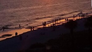 Een strand bij zonsondergang, mensen wandelen langs de kust.