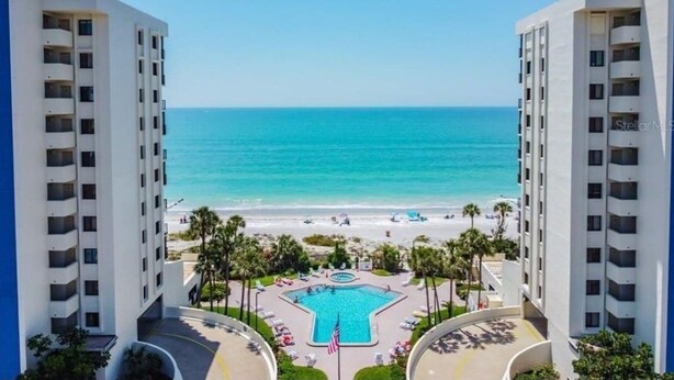 Een resort met een centraal gelegen zwembad, uitzicht op het strand en een heldere lucht.