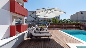 A rooftop pool area with lounge chairs and a large umbrella. - Apartment house Ivan John (Podstrana)