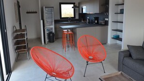 A modern kitchen with a central island, two orange chairs, a grey sofa, and a dining area with a small table. - Comfortable 3-bedroom villa 500 metres from LOZARI beach (Palasca)