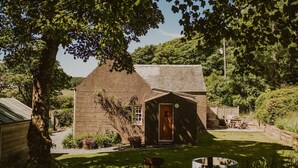 Ein rustikales Haus mit Holztür, einer kleinen Veranda und einem Garten mit Tisch und Stühlen.