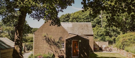 A rustic house with a wooden door, a small porch, and a garden area with a table and chairs.