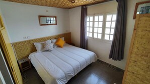 A bedroom with a bed, a headboard, a window with curtains, a wall-mounted mirror, and a door. - BigBlue Hostel Surf & Coworking (Taghazout)