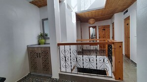 A narrow hallway with a wooden cabinet, a potted plant, and a staircase with a wrought iron railing. - BigBlue Hostel Surf & Coworking (Taghazout)