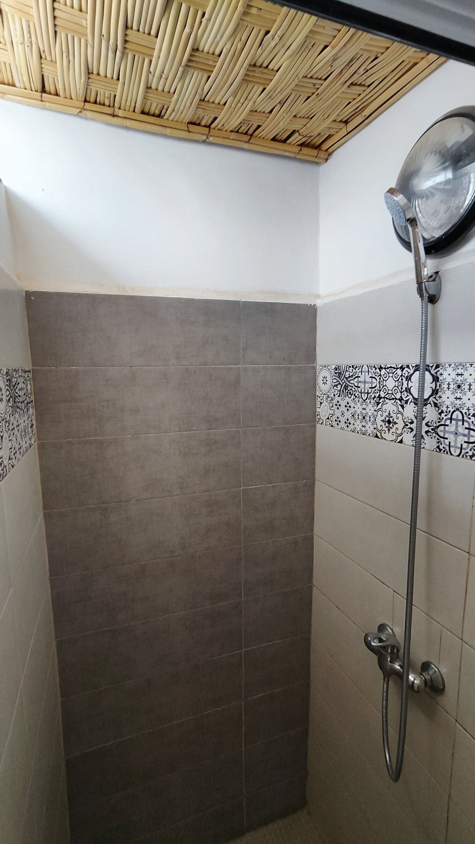 A shower with a bamboo ceiling, grey tiles, and patterned tiles on the walls.