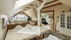 A spacious living area with a high ceiling, wooden beams, a large dining table, and a view of the sea. - Strandhaus Brunhild (Timmendorfer Strand)