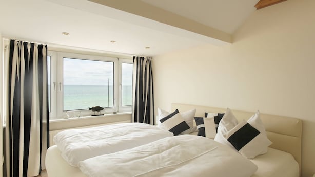 A bedroom with a large bed, a window with curtains, and a view of the sea. - Strandhaus Brunhild (Timmendorfer Strand)