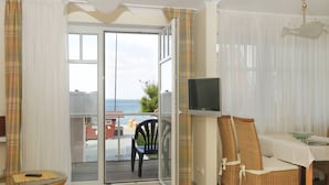 A room with a sliding glass door leading to a balcony, a television mounted on the wall, and a dining area with wicker chairs and a table. - Strandhaus Brunhild (Timmendorfer Strand)