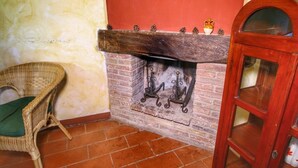 Ein rustikaler Raum mit Kamin aus Backstein, einem Korbstuhl und einem Holzschrank.