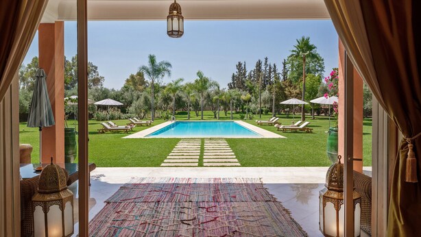 A view of a swimming pool with lounge chairs and umbrellas, surrounded by greenery and palm trees. - NEYLLA (Marrakech)