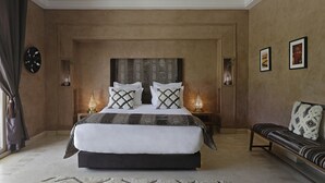 A large bed with a patterned headboard, bedside lamps, a bench, and framed artwork on the walls. - NEYLLA (Marrakech)